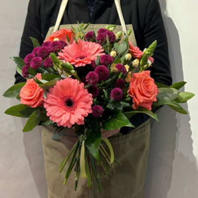 Coral Burst - This stunning arrangement bursts with bold coral gerberas, rich raspberry chrysanthemums, and fresh coral roses, creating a lively mix of colour and texture. Accented with soft cream buds and lush greenery.